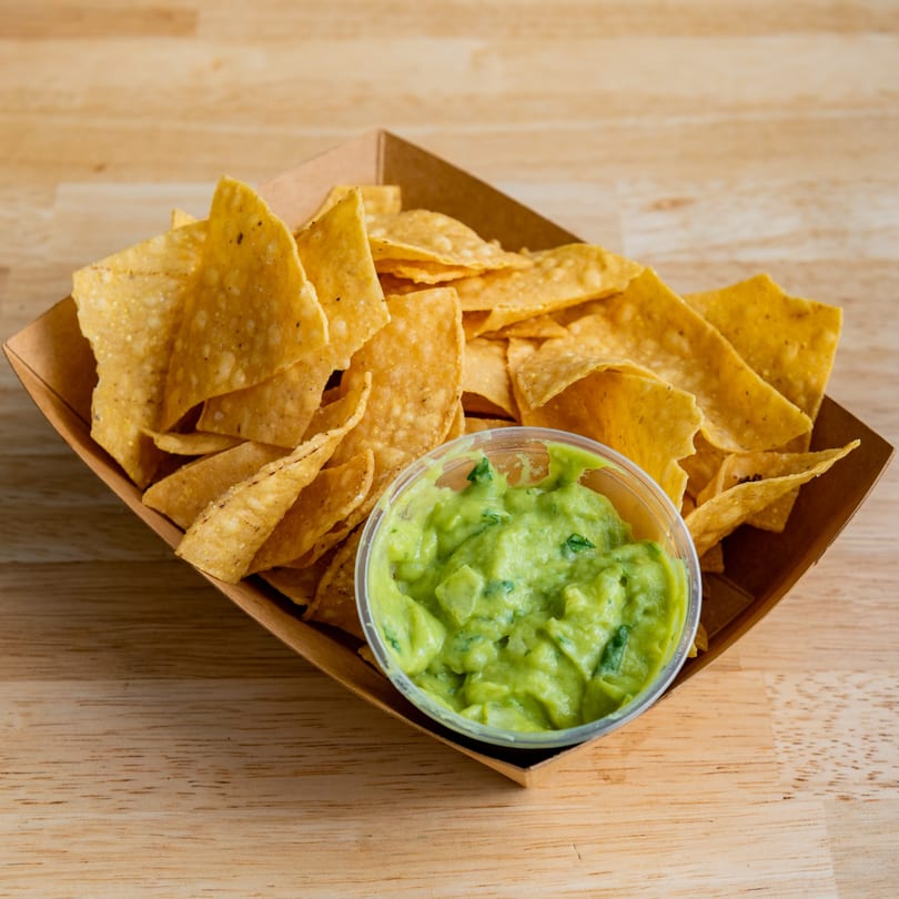 El Barrio Neighborhood Tacos' crispy tortilla chips and a side of fresh guacamole in a paper tray.