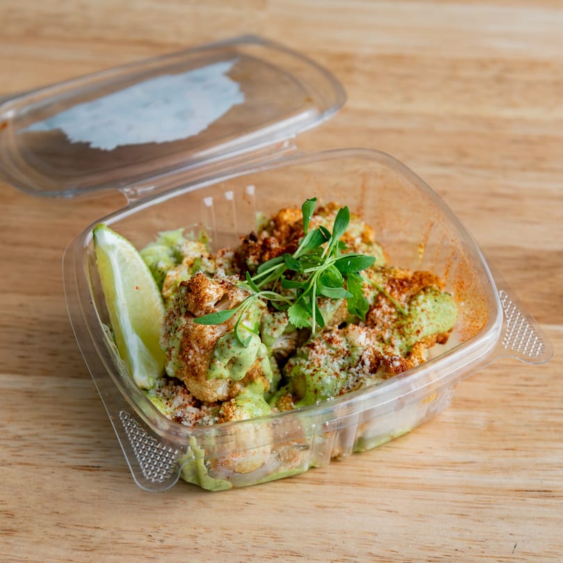 El Barrio's Mexican cauliflower bites with green sauce, spices, and a lime wedge in a to-go container.